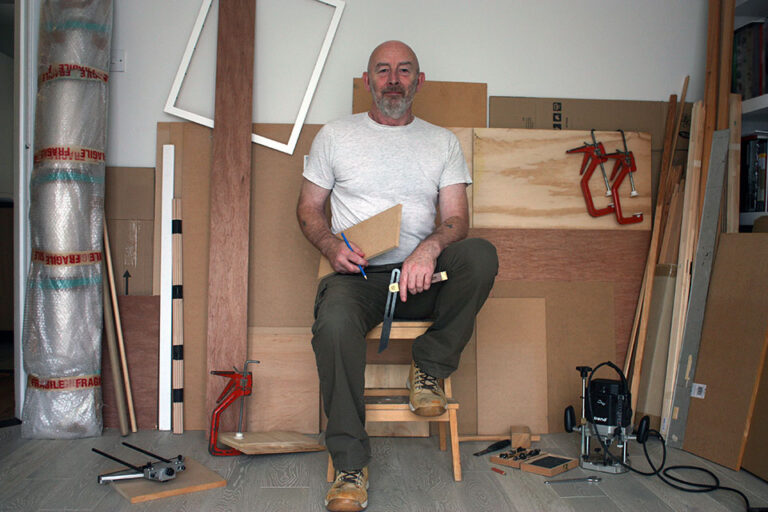Phil Illingworth sat on a stool in his studio